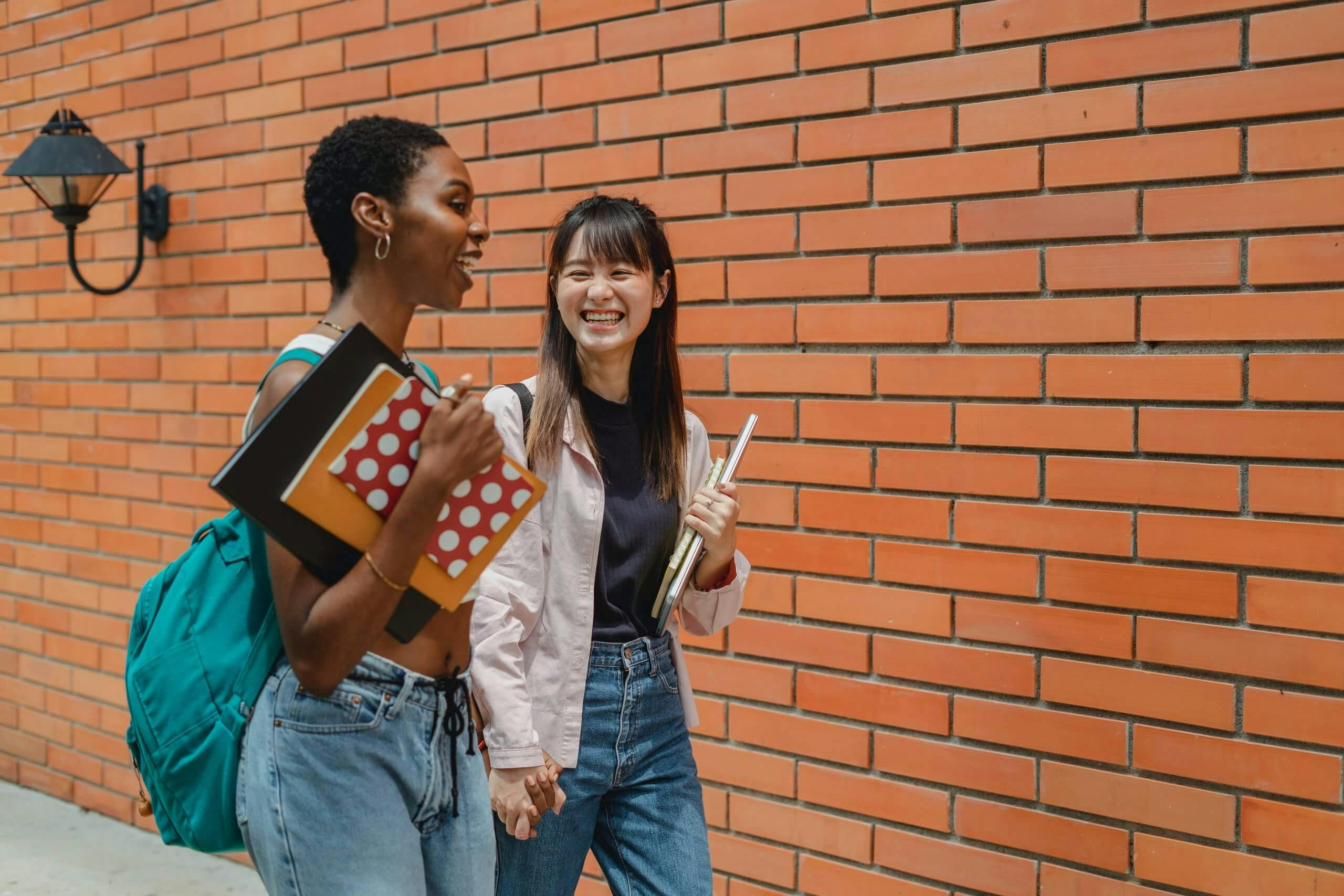 two female students walking and talking alongside brick wall