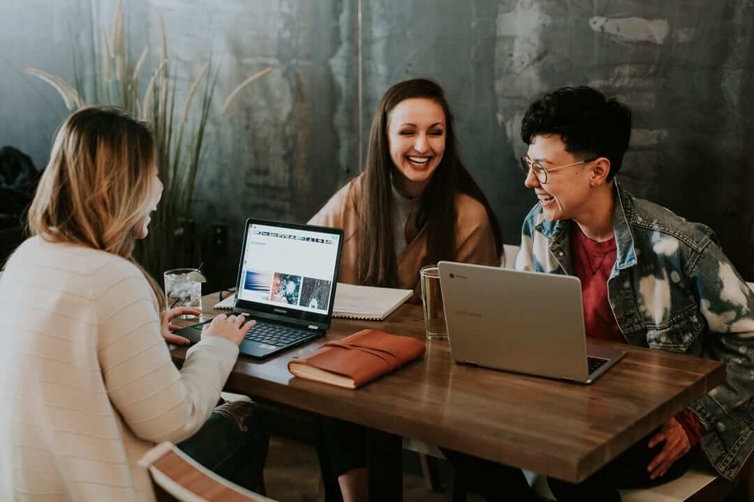 three people working around table on laptops