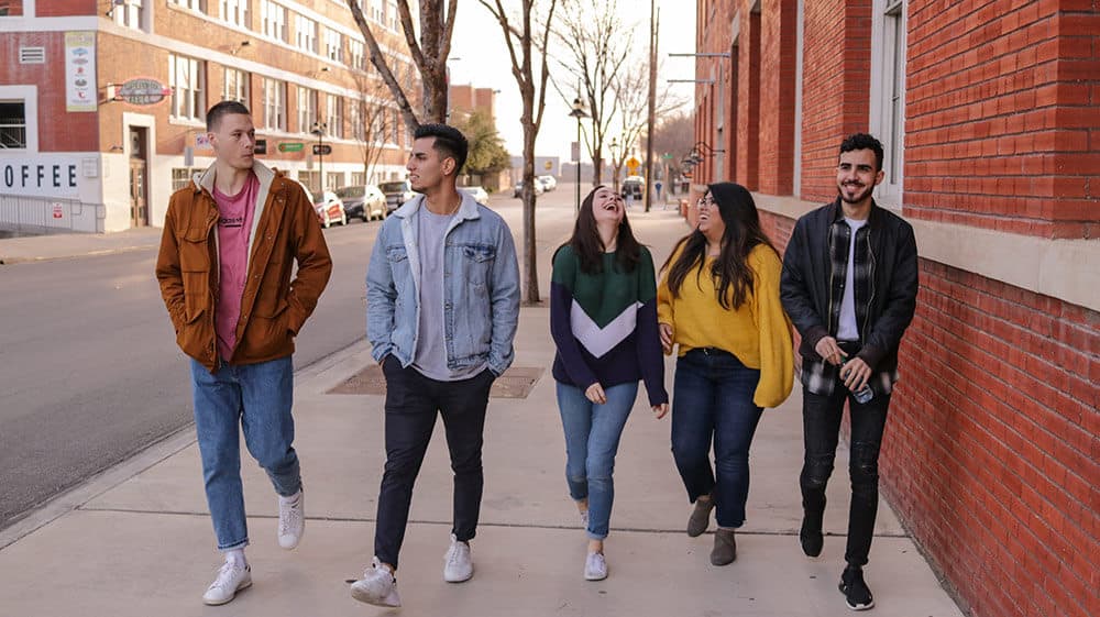 group of five students walking down urban street with red brick buildings