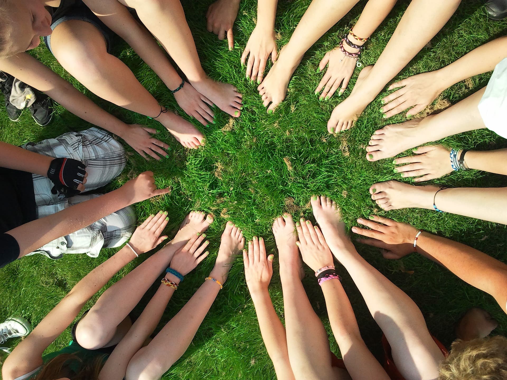 group of people with bare arms and legs in a circle outside on grass