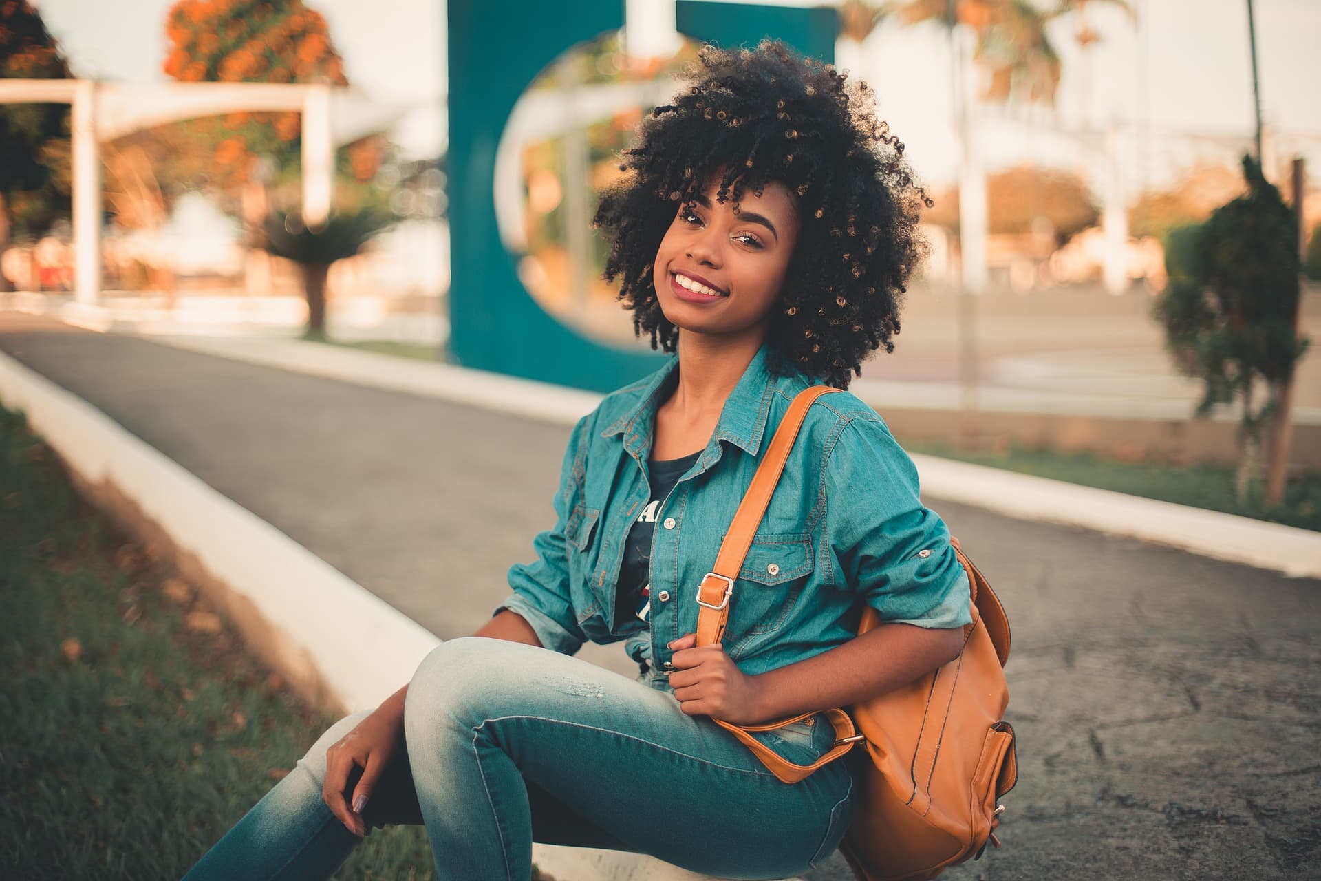 student sitting on curb with backpack smilingg