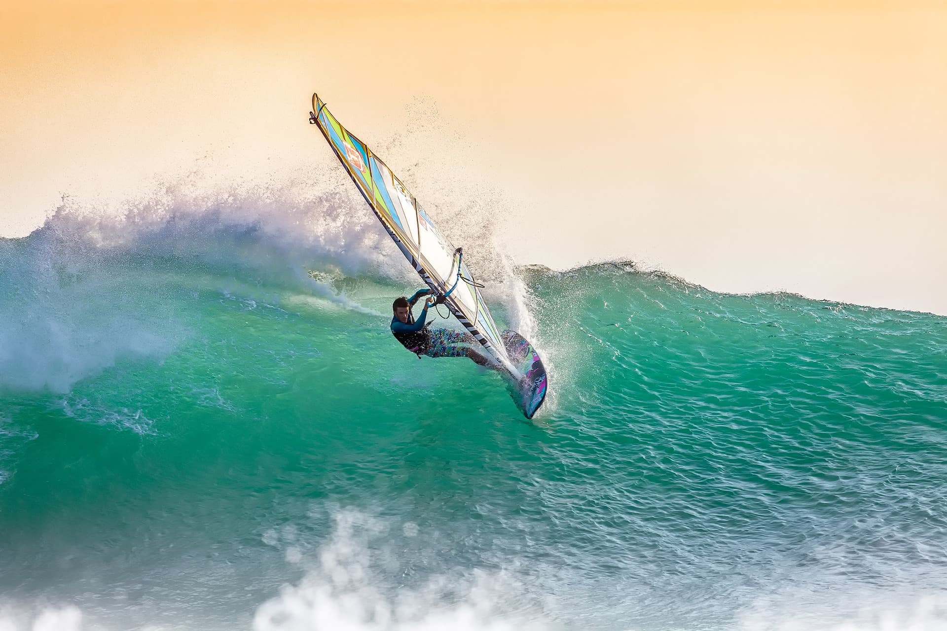 windsurfer riding turquoise wave against golden sky