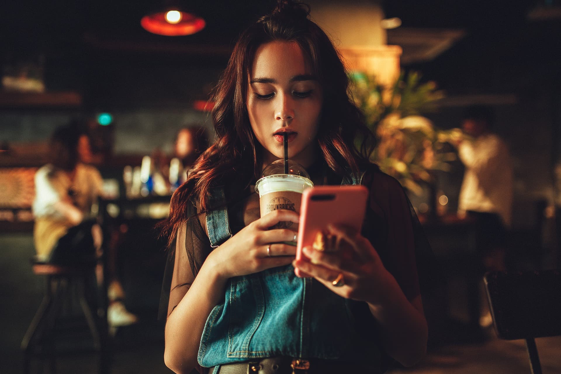 woman sipping frozen drink through straw while looking at phone