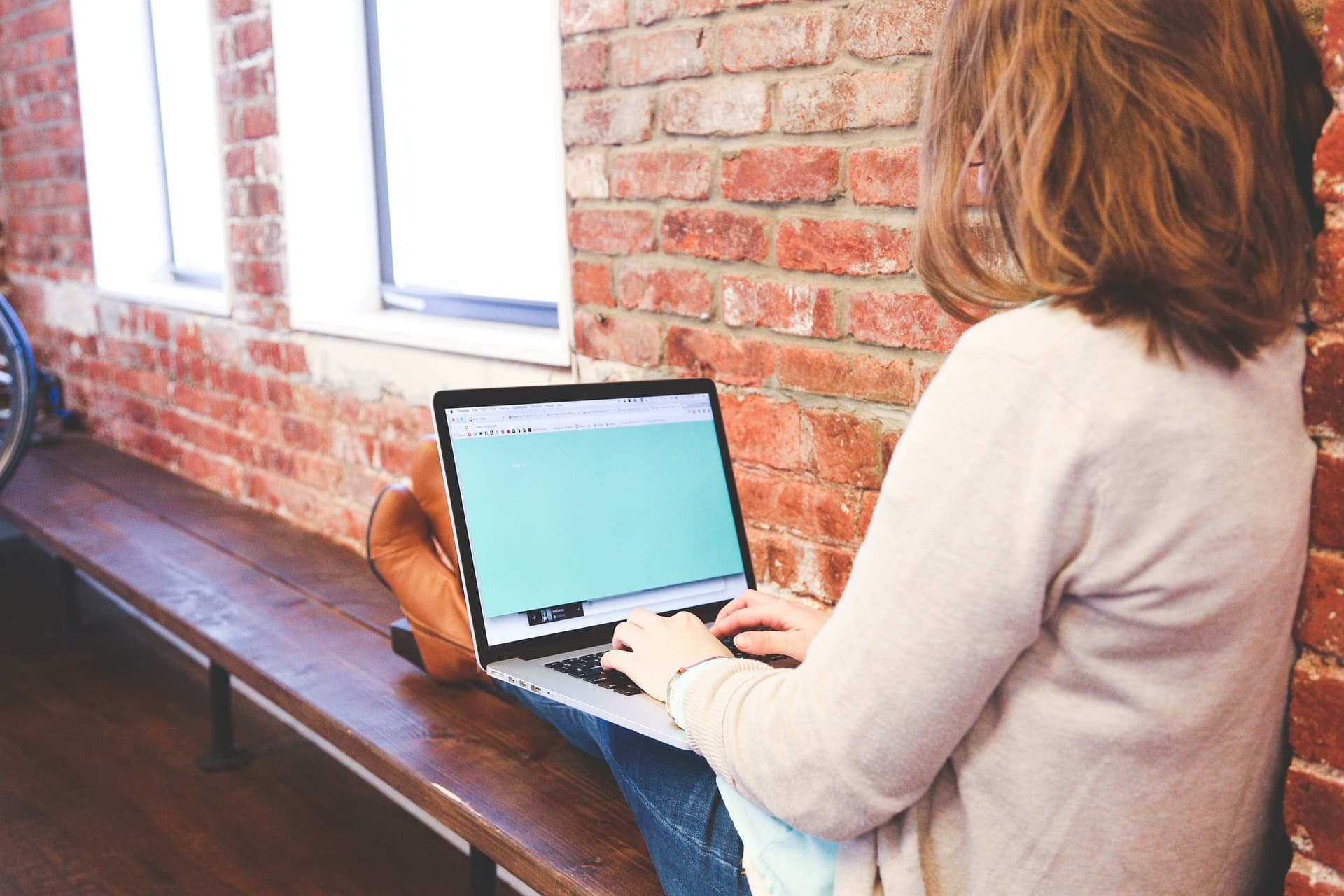 woman sitting across bench typing on laptop