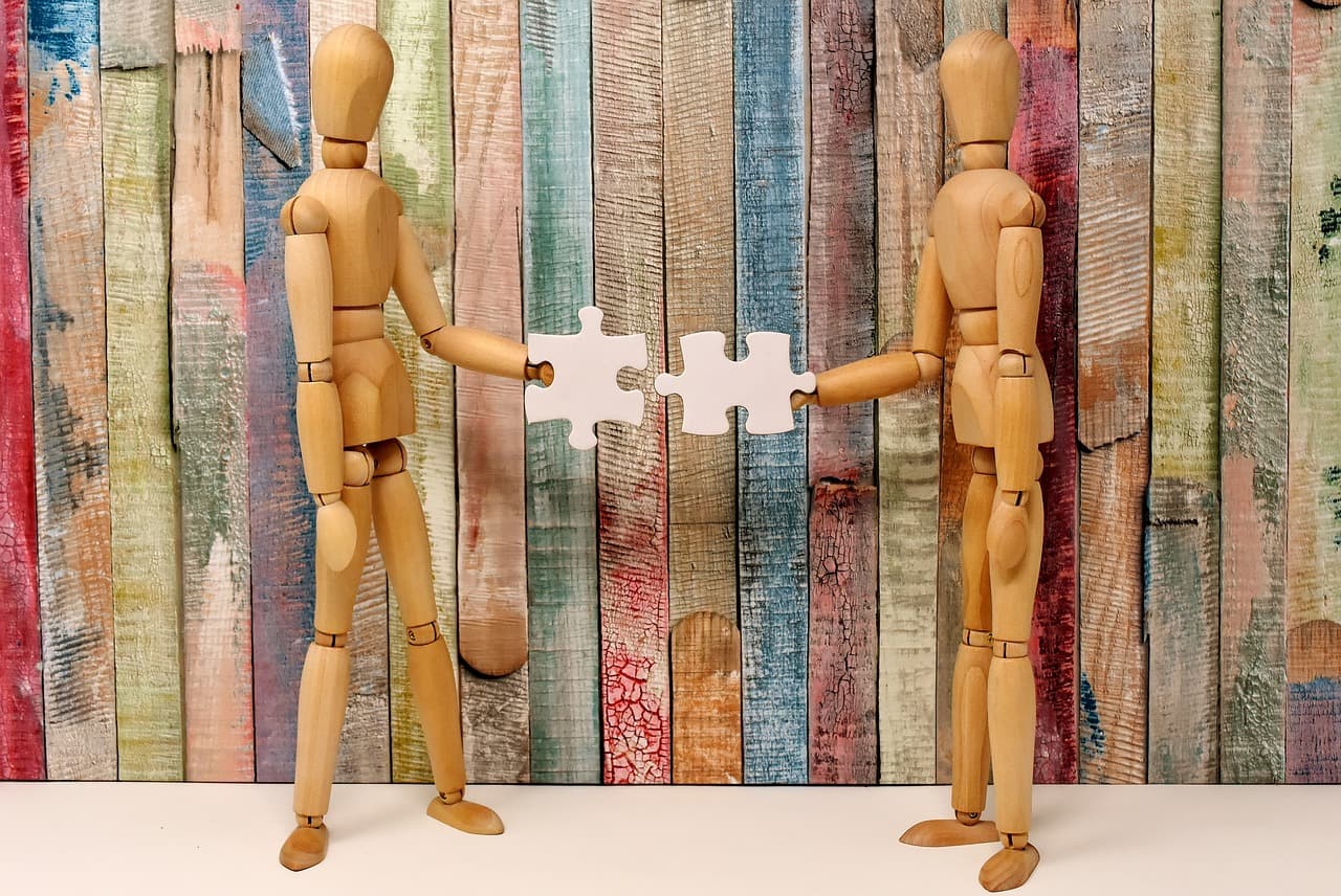 Two marionettes connecting two puzzle pieces against a popsicle stick background