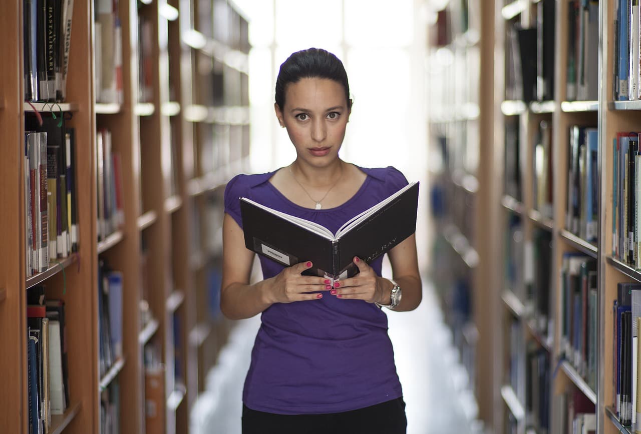 woman reading book in library stacks