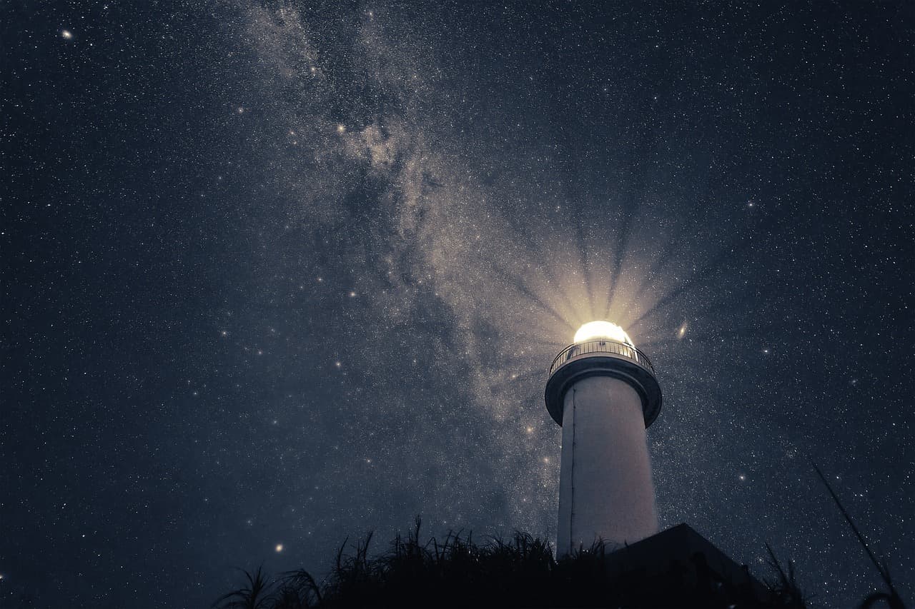 illuminated lighthouse below starry sky