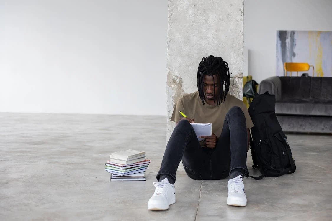 Man sitting against post inside writing in notebook