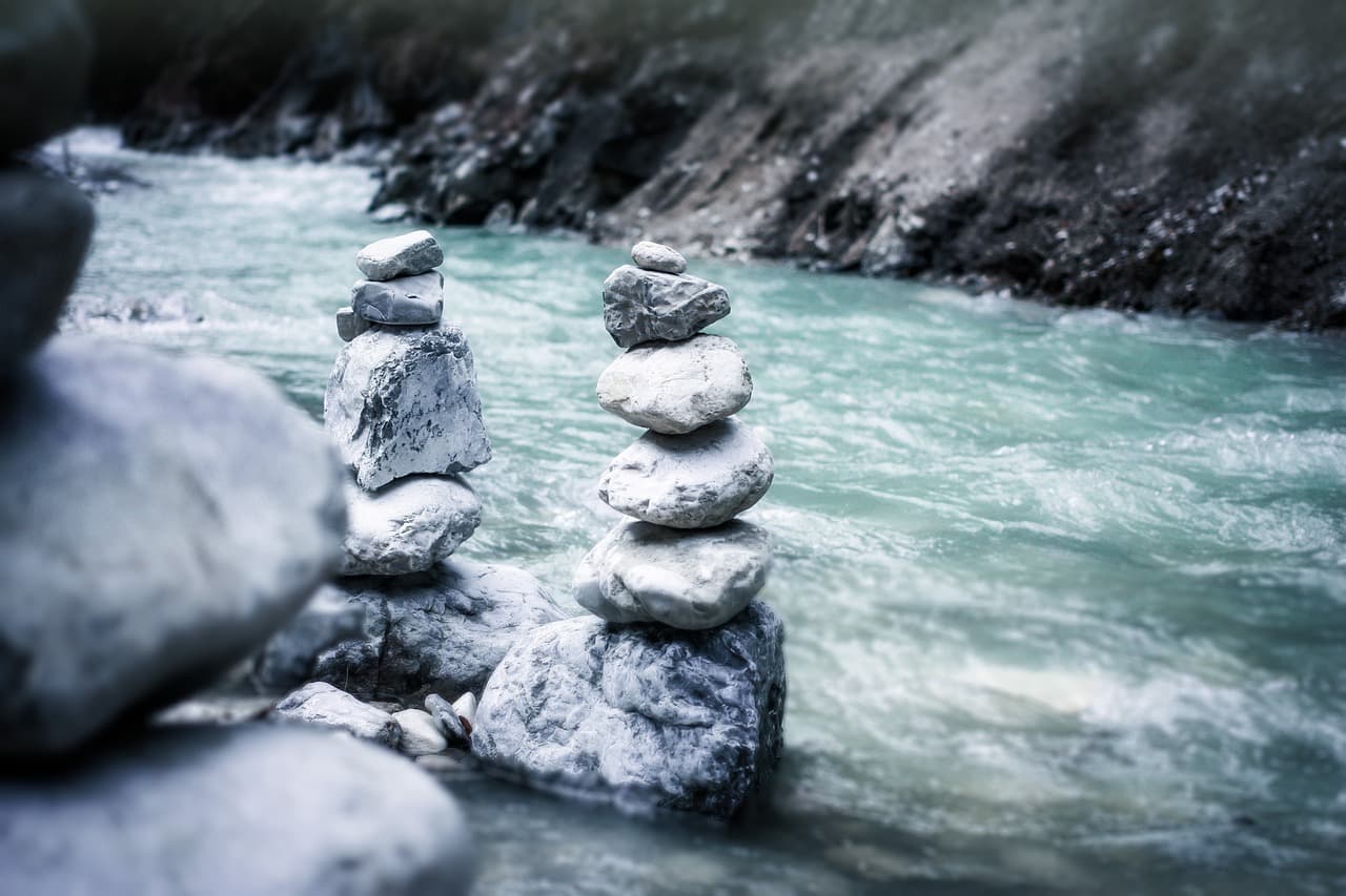 two stacks of balanced rocks amid raging river