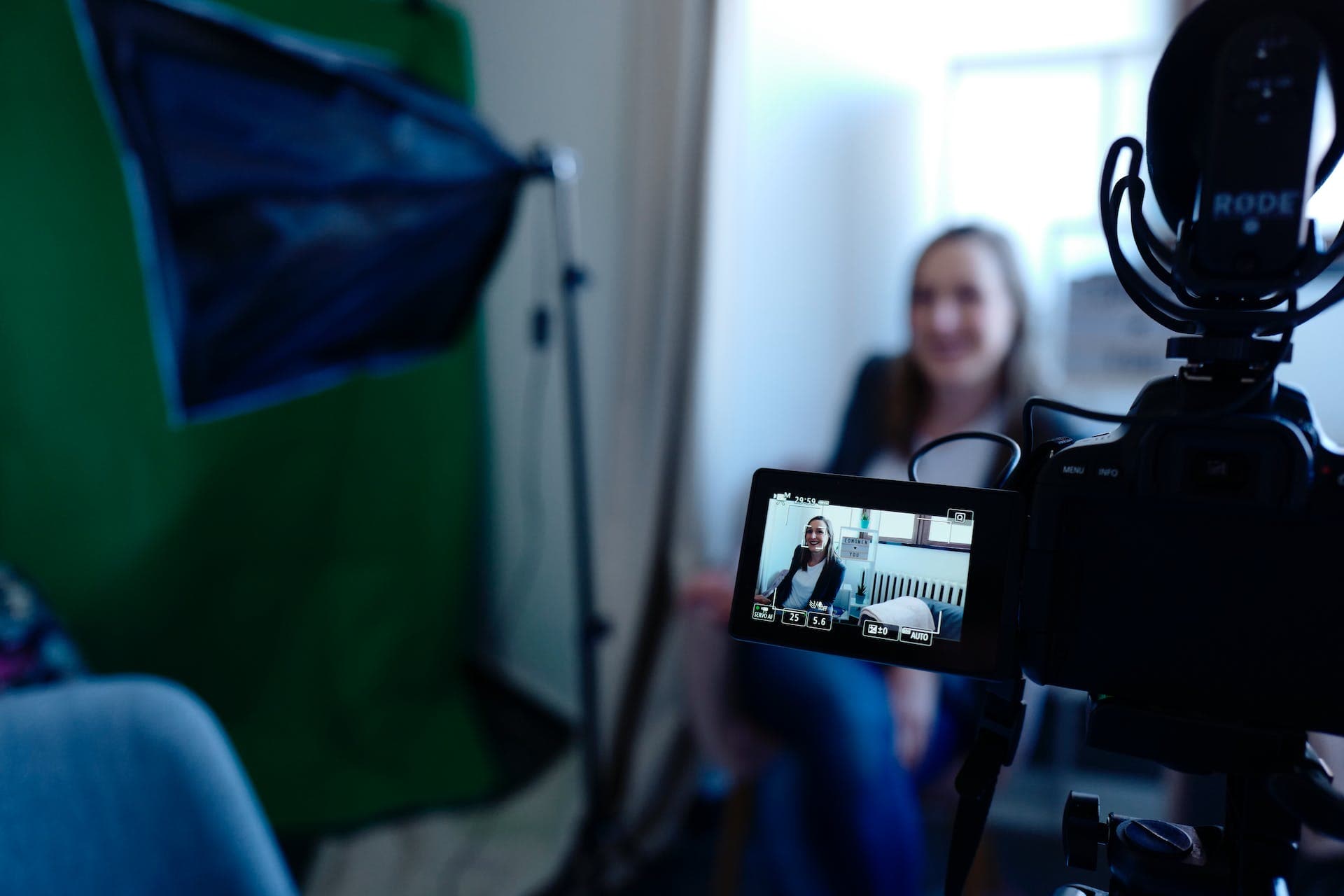 sitting woman in background being filmed interview-style with camera gear in foreground