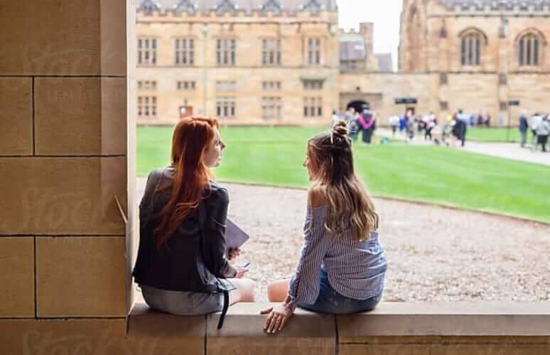 two students seated conversing by quad