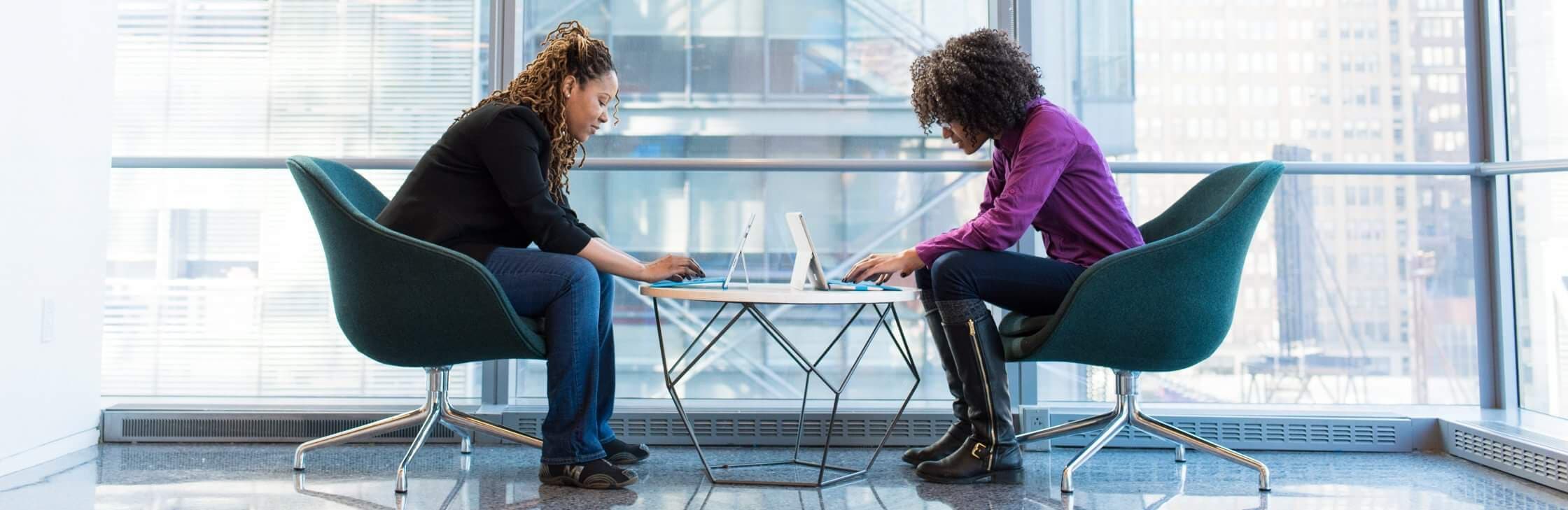 two women working on laptops across from each other at coffee table