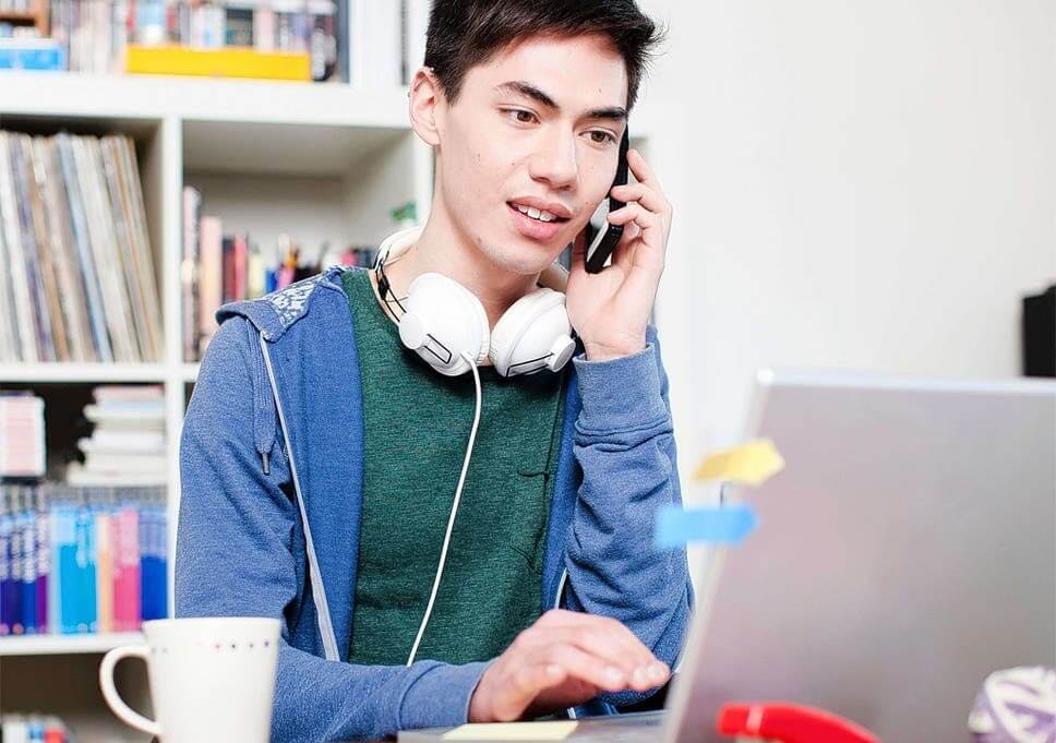 man working at laptop with headphones around neck talking on phone