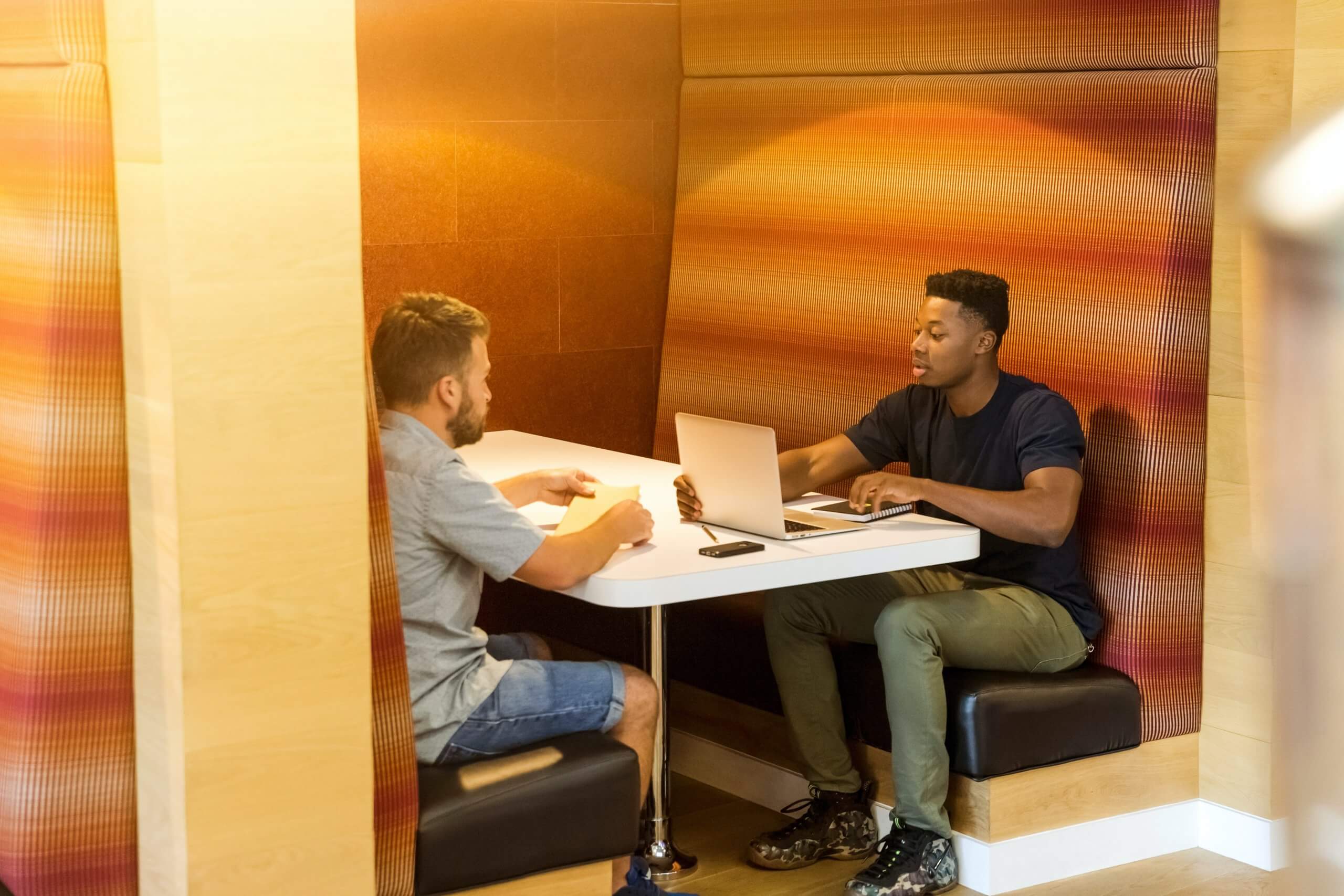 two men working in booth off single laptop