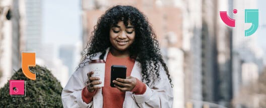 woman with coffee walking outside looking at phone