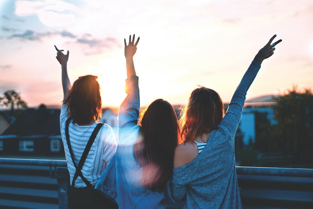 three women waving at sunset over houses