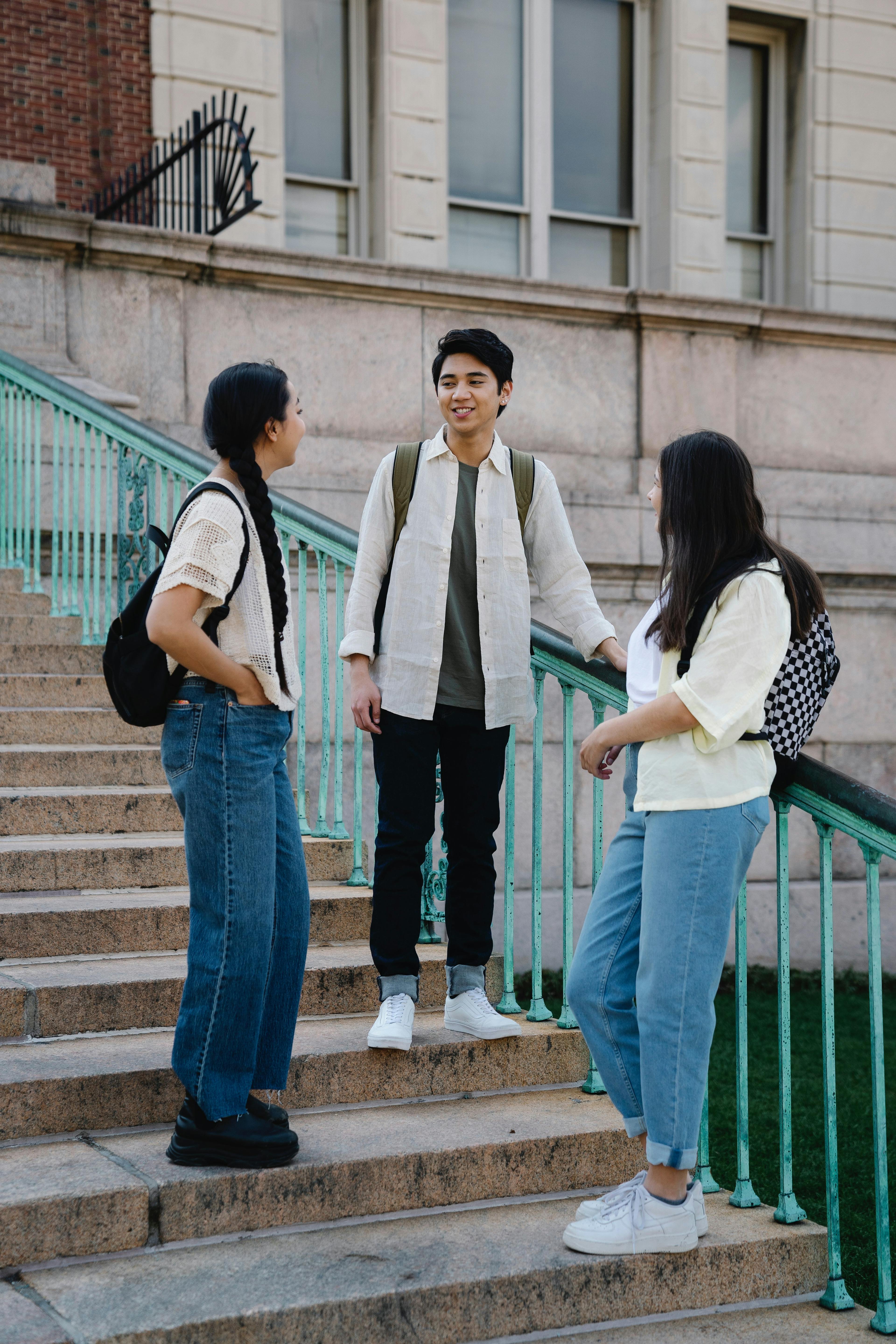 three students wearing backpacks speaking on steps
