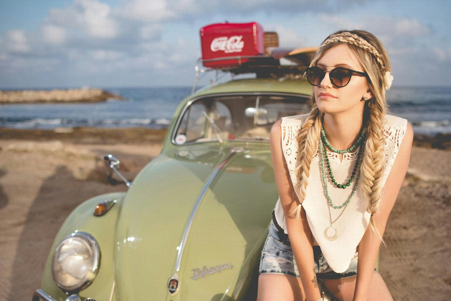 woman with sunglasses sitting on hood of vintage VW Beetle by the sea