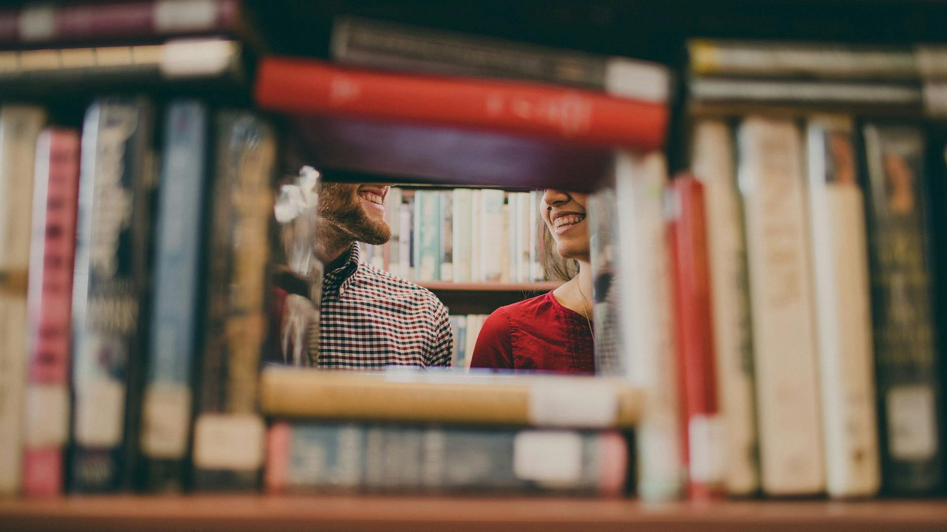 two students smiling visible through gap in library stacks